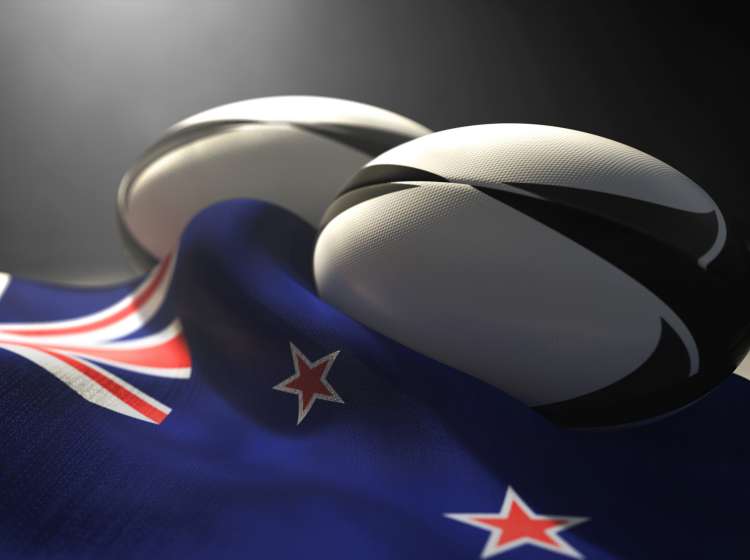 Two regular rugby balls with color design elements resting on a draped new zealand flag on an isolated dark studio background - 3D render