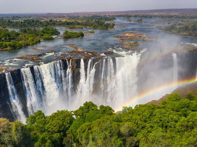 Aerial few of the world famous Victoria Falls with a large rainbow over the falls. This is right at the border between Zambia and Zimbabwe in Southern Africa. The mighty Victoria Falls at Zambezi river are one of the most visited touristic places in Africa.