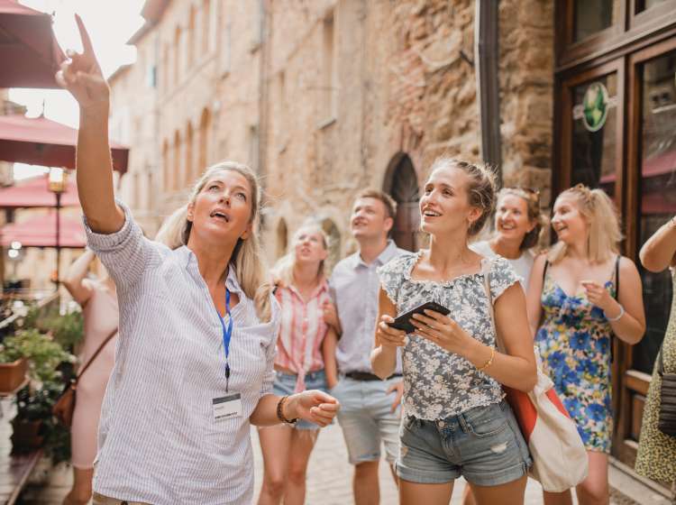 Medium group of people standing in a street in Volterra. They're listening to a tour guide who is talking about the architecture and the history.