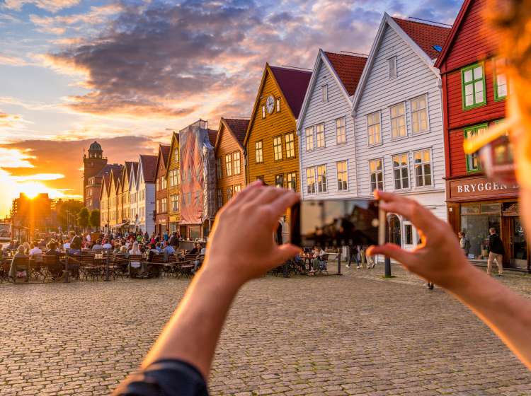 Tourist photographing Bryggen at sunset with smartphone, Bergen, Hordaland County, Norway