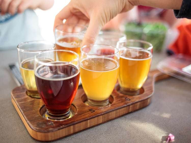 A hand lifts a glass from a flight of six beers on a wooden paddle