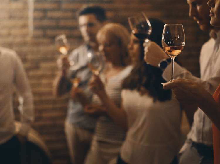 Closeup side veiw of group of adults during wine tasting in a wine cellar. There are three women and three men tasting different kinds of wines, selective focus. Low key.