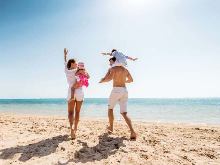 Cheerful parents enjoying at the beach with their little children. Man is carrying little boy on his shoulders. Copy space.