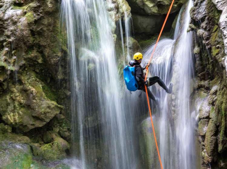 Canyoneering member with backpack rappeling down the waterfall in the canyon.