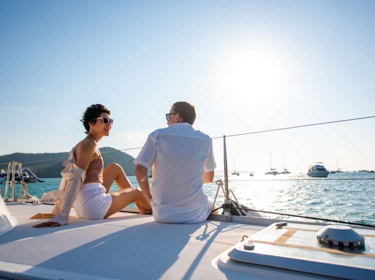 Caucasian couple enjoy outdoor luxury party drinking champagne with talking together while catamaran boat sailing at sunset. Man and woman relax with outdoor lifestyle sail yacht on summer travel vacation