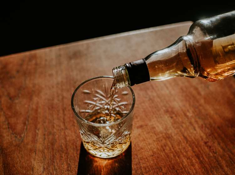 A bottle of whisky is poured into a cut glass tumbler over ice. Space for copy.