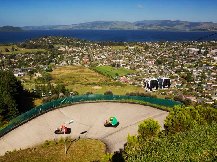 Rotorua, New Zealand - January 7, 2013: Two people head down a track in luges, while Skyline Rotorua gondolas operate beside them, heading towards the summit of Mt Ngongotaha.