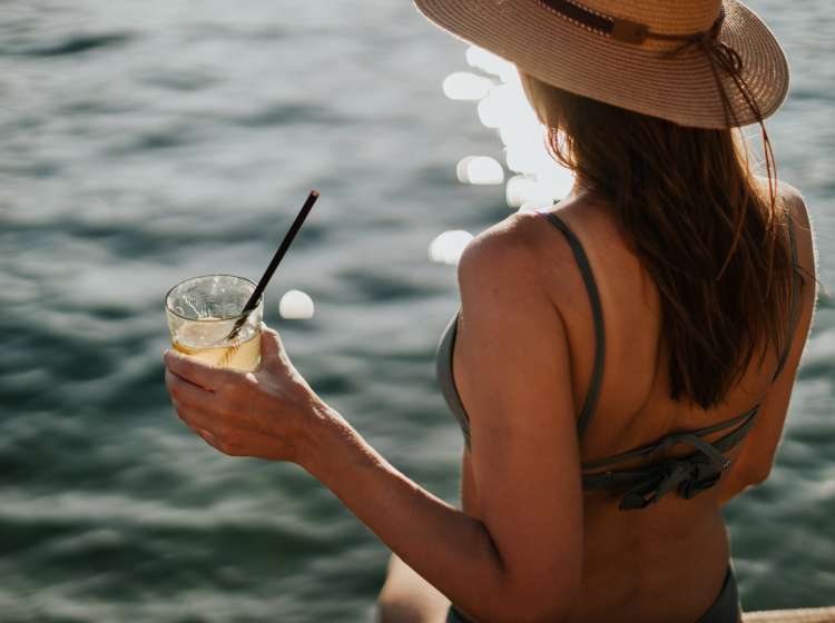 Young woman wearing a hat and bikini drinking cocktail in a beach bar during her vacation in Kotor Bay