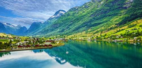  Big green mountains next to water and houses 