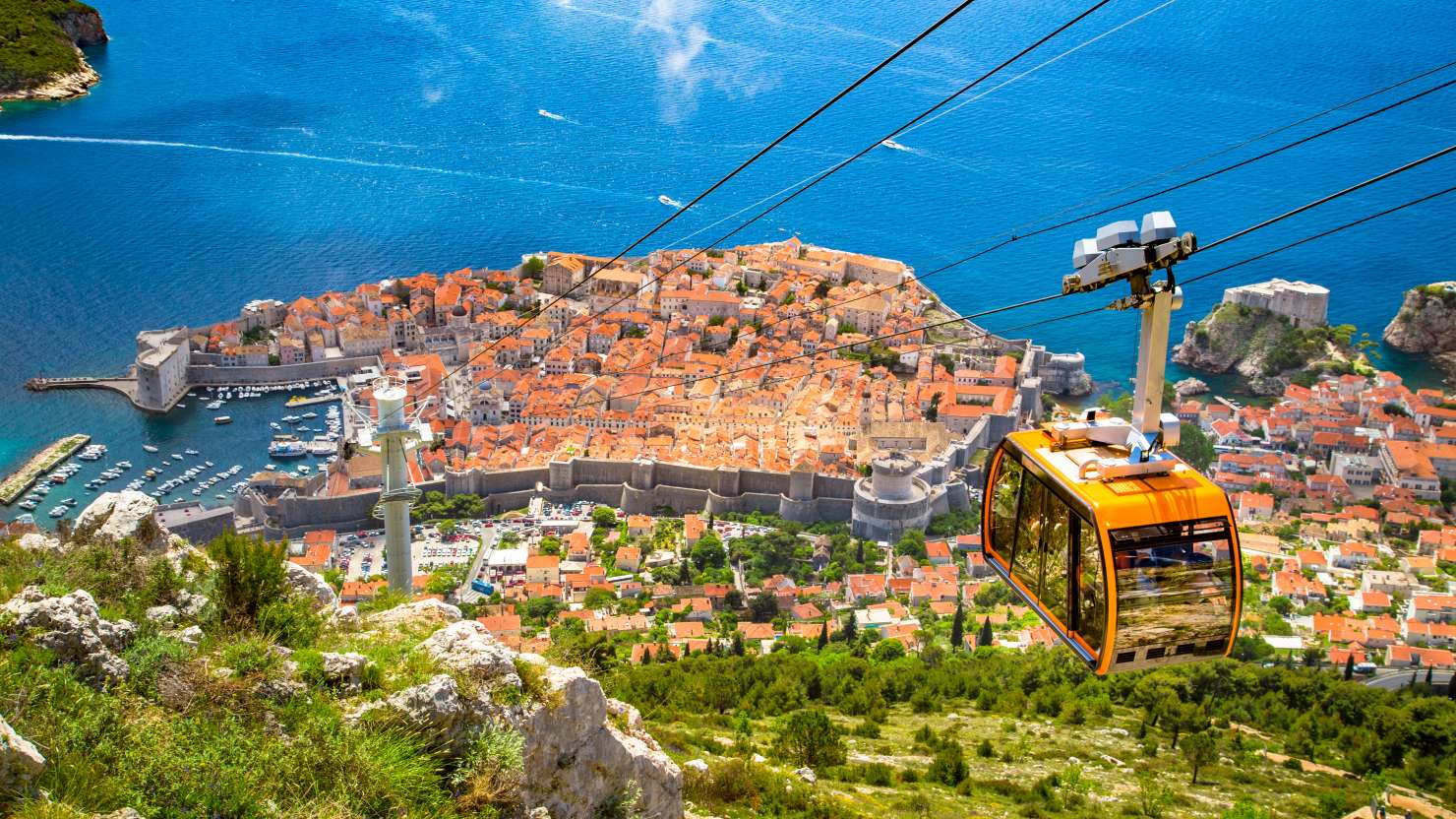 Aerial panoramic view of the old town of Dubrovnik with famous Cable Car on Srd mountain on a sunny day with blue sky and clouds in summer, Dalmatia, Croatia