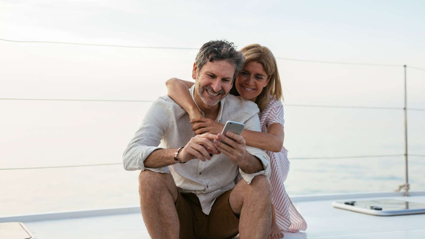 Mature couple looking at smartphone, sitting on a sailing boat