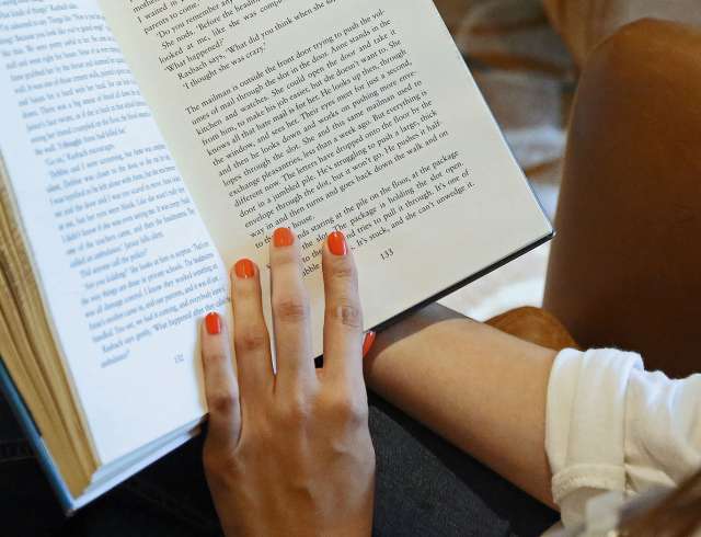 Female hand with red-painted nails holding open a book