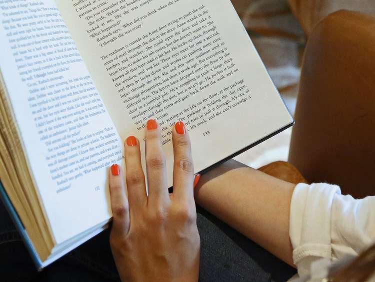 Female hand with red-painted nails holding open a book