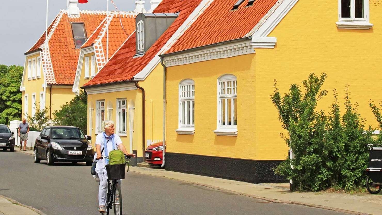 Woman cycling past yellow house with orange roof in Skagen